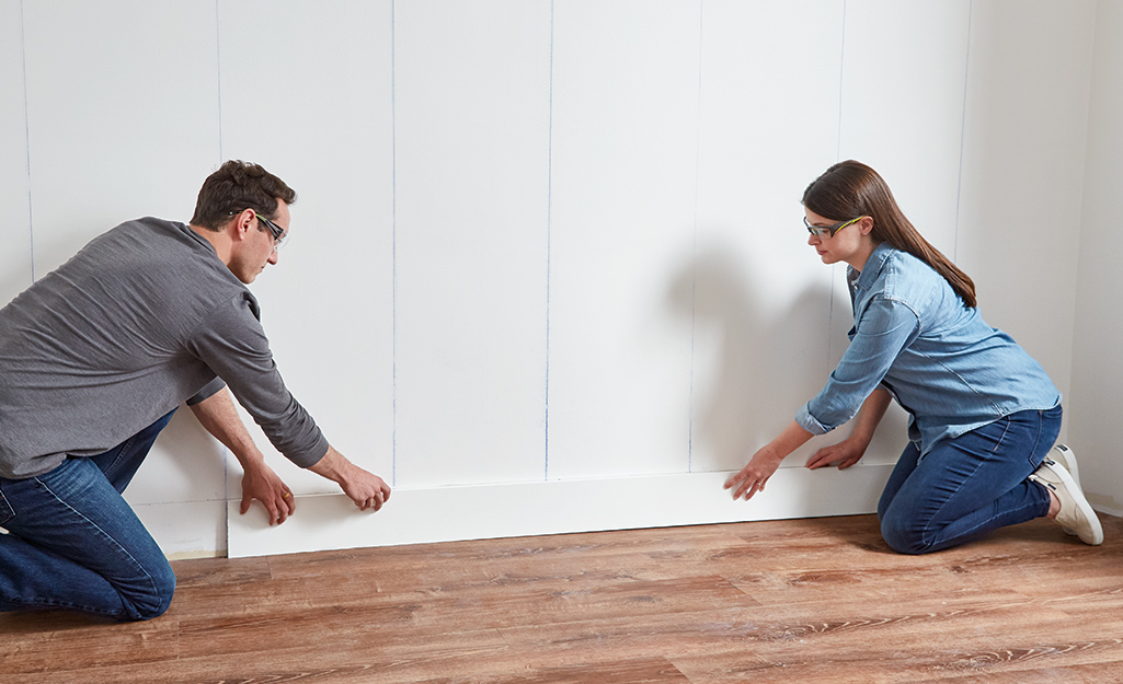 Couple lining up first the shiplap board on a wall.
