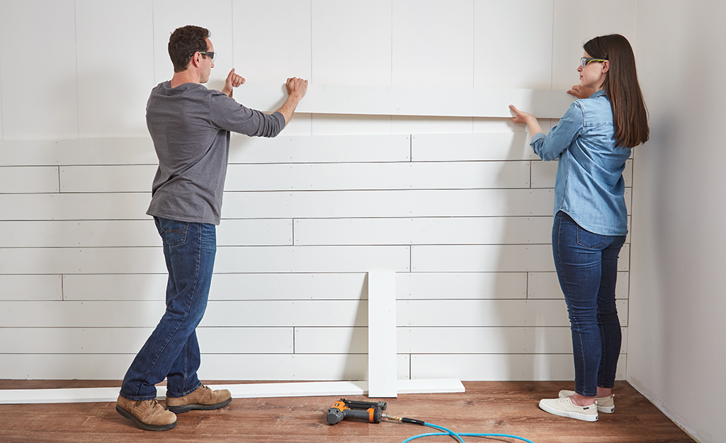Couple adding shiplap board to a wall that's almost complete.