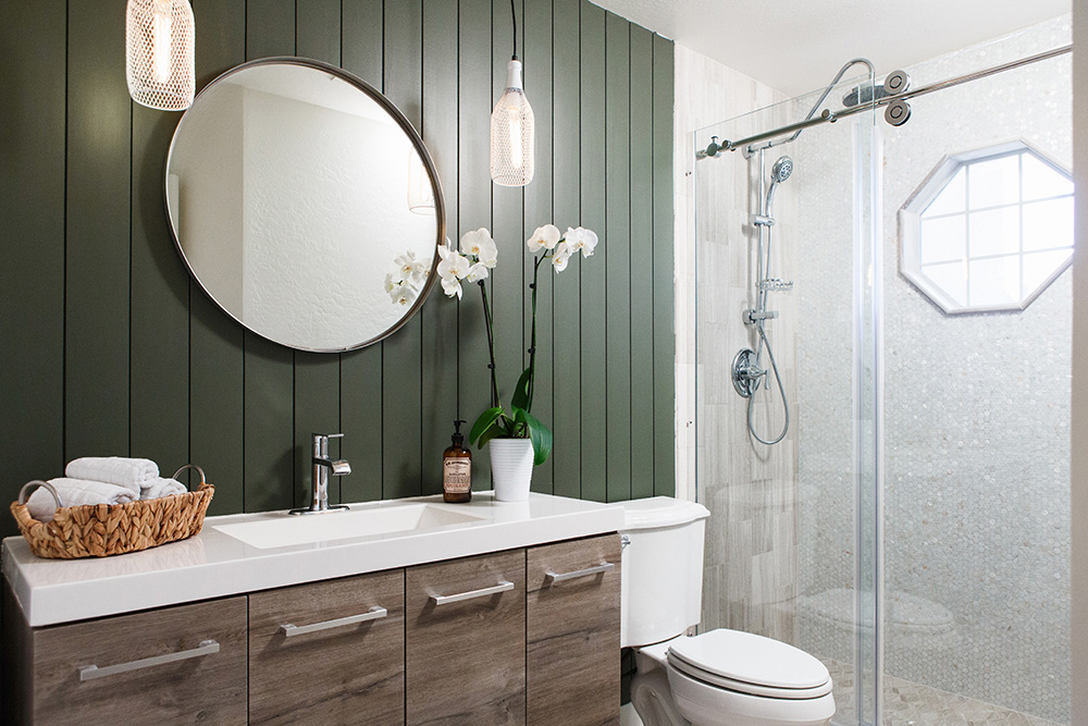 A renovated bathroom with green vertical shiplap walls and a floating wood vanity with four silver bar pulls.
