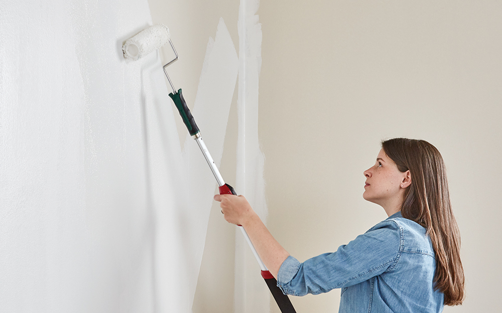 Woman painting wall with a roller.
