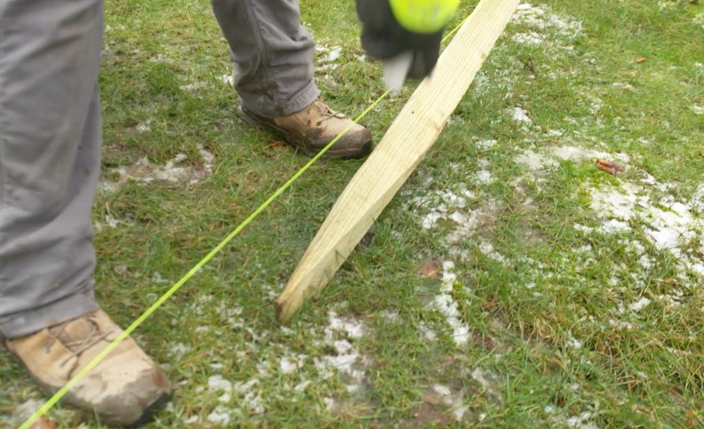 A person laying out a fence post along a string border.