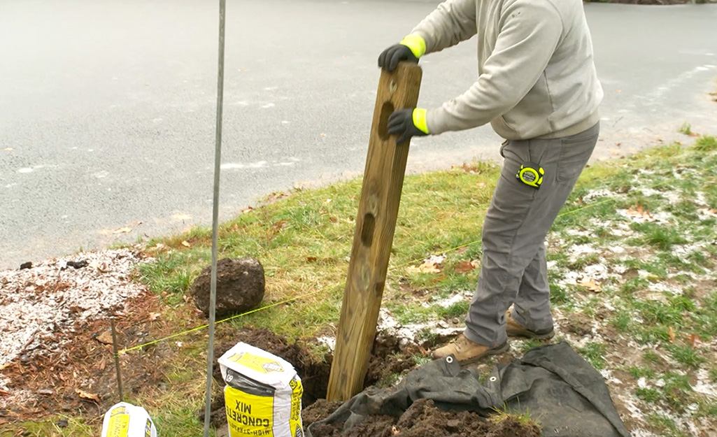 A person setting a post of a split rail fence in a hole.