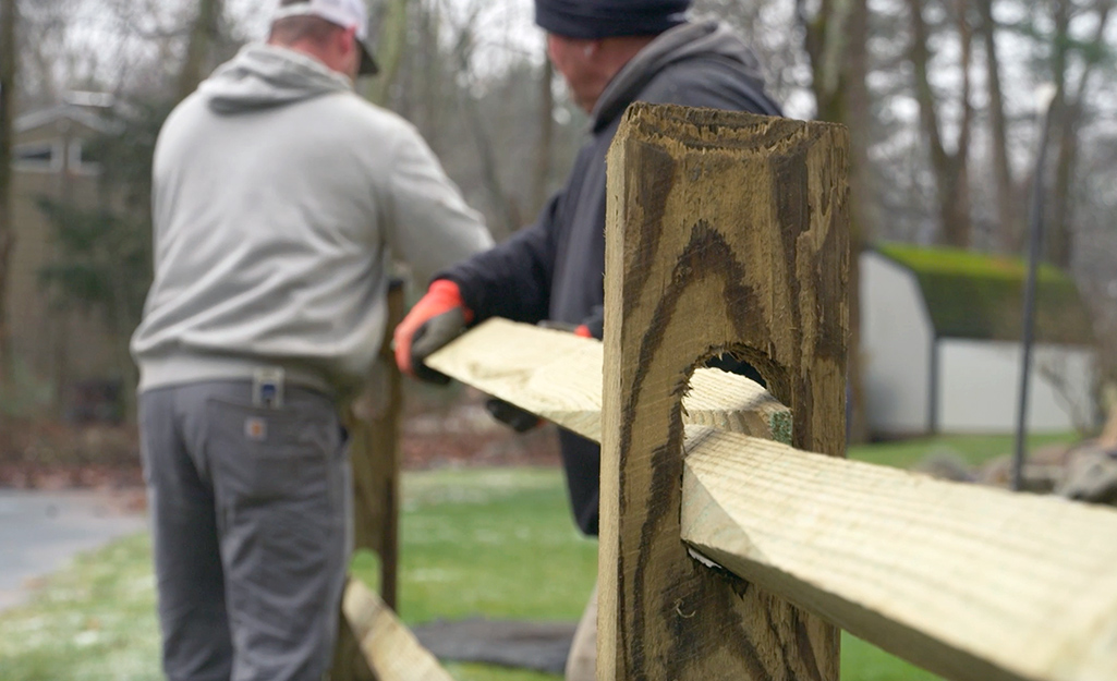 Two people setting the top rail of a fence section.