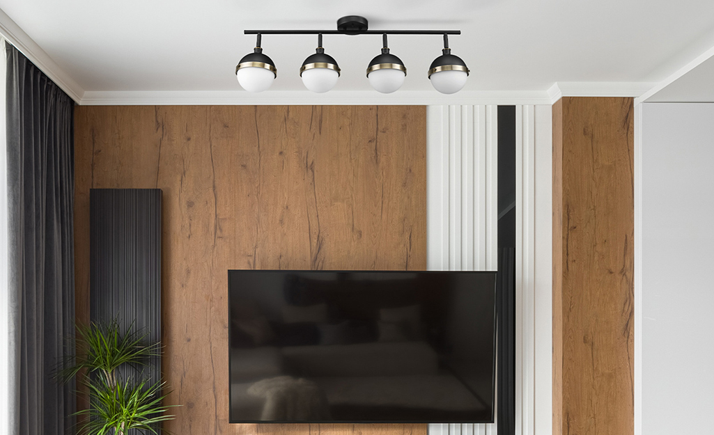 Four rounded track lights hang from a track on the ceiling of a wood-paneled room. Four rounded track lights hang from a track on the ceiling of a wood-paneled room.