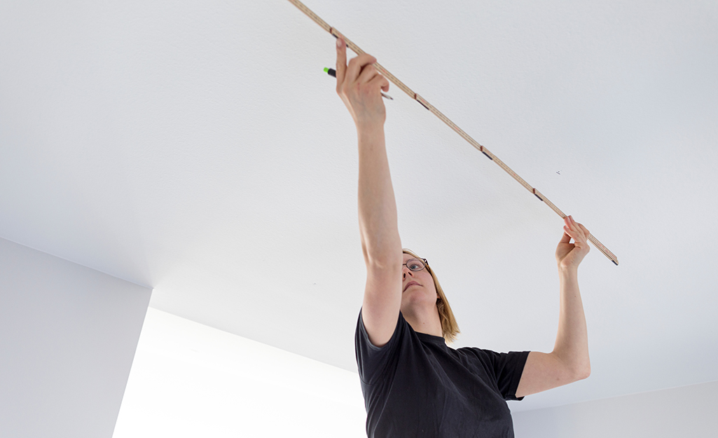 A person measures the ceiling before installing track lights.