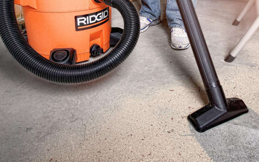A person uses a vacuum to clean a concrete floor.