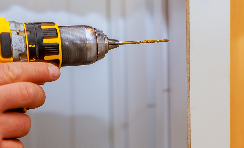 A person drills a cabinet screw.