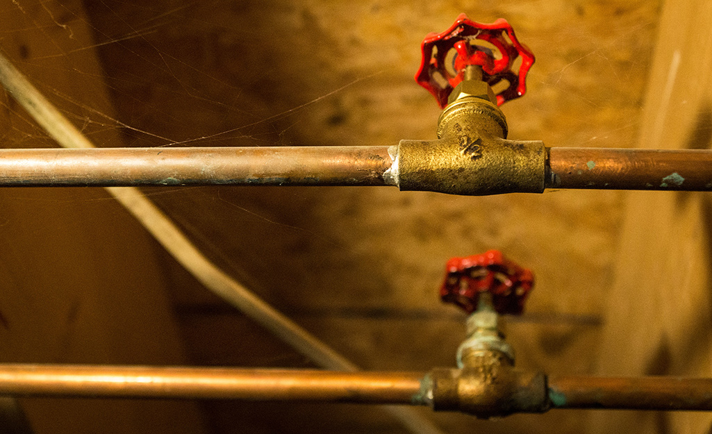 Main water supply shut-off valves on copper pipe in a basement.