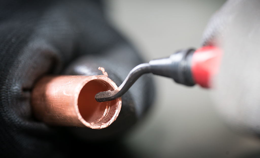A person using a deburring tool to remove burrs from a cut copper pipe.