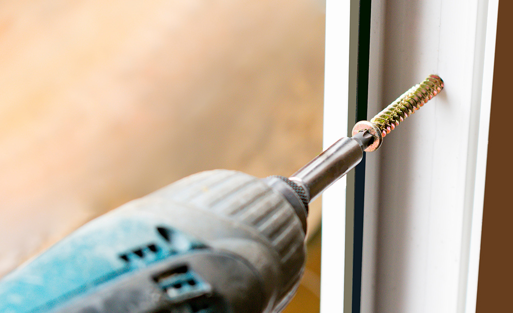 A screwdriver drills a screw into a window track.