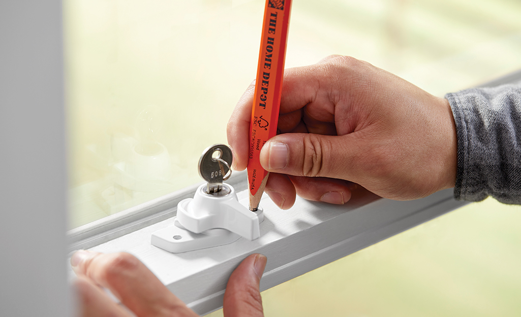 A person uses a pencil to mark the place where a new window lock should be installed.
