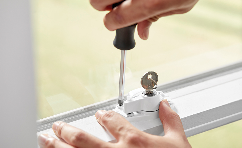 A person uses a screwdriver while installing a window lock with a key.