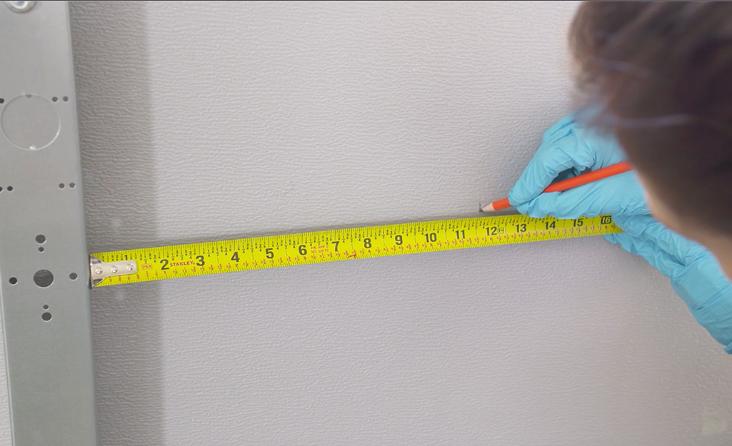 A person marking a garage door panel at the 12-inch measurement on a steel measuring tape.