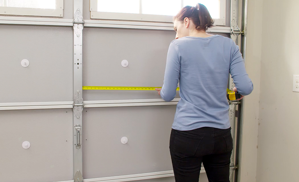 A person measuring the length of a garage door panel.