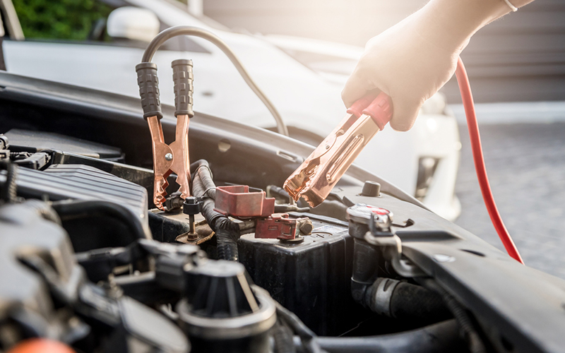 person's hand removing jumper cables from a car battery
