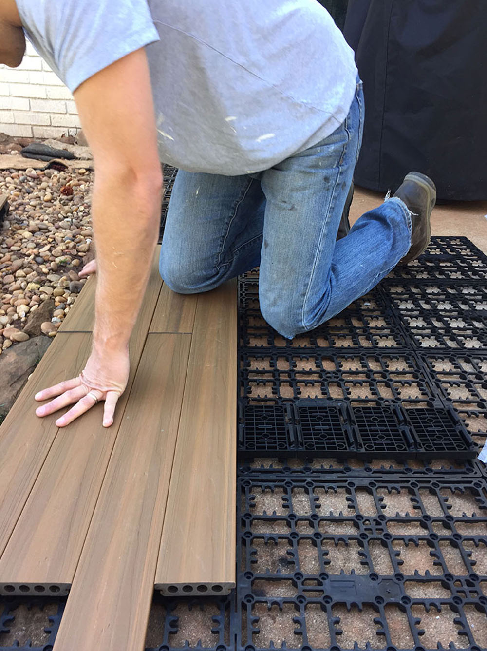 A person snapping in deck boards over a concrete patio.