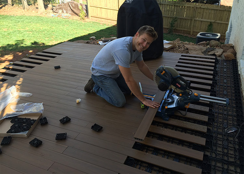 A man smiles for the camera while installing deck boards.
