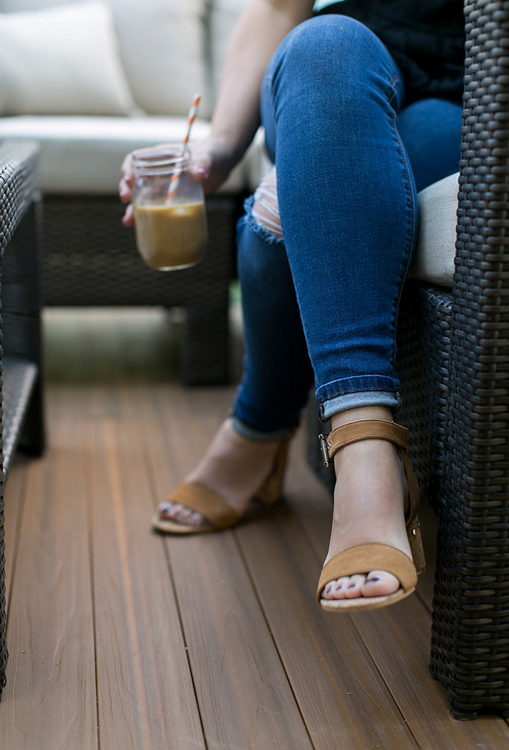 A person wearing jeans and sandals sits on a patio with a drink. 