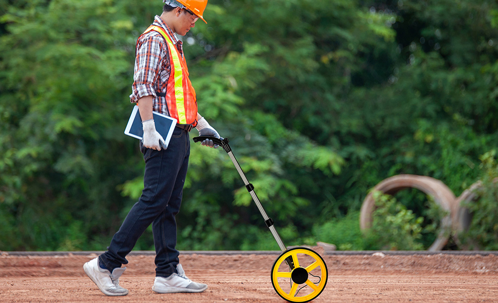 Someone measures a bare yard for sod with a measuring wheel.