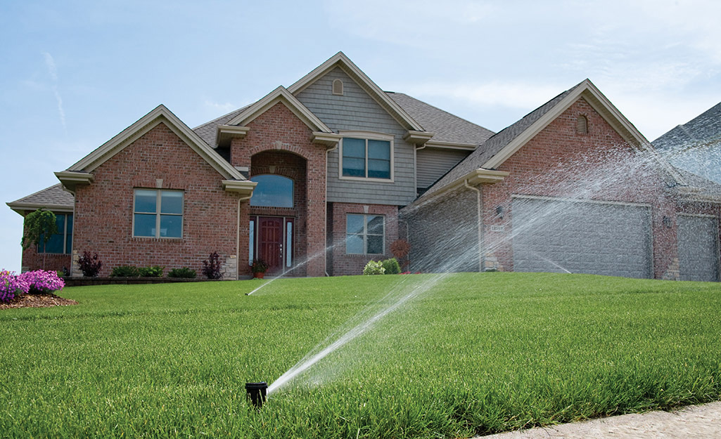 Sprinklers water a green lawn in front of a house.