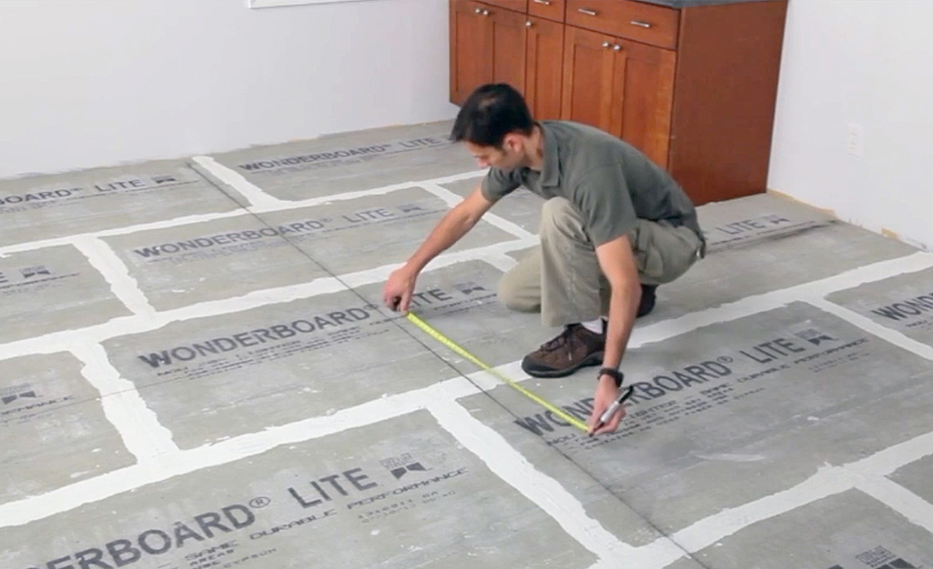 A man measures and marks gridlines for tile layout.