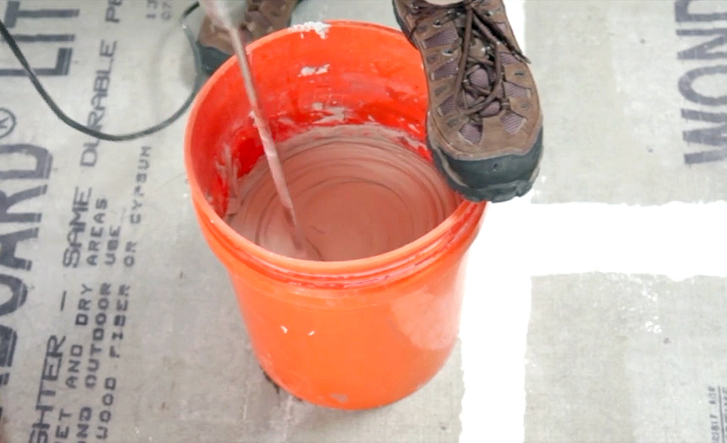 A person mixes grout mortar in a bucket.