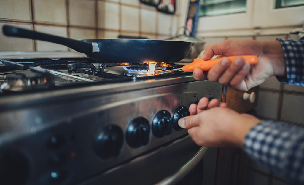 A person uses a long lighter to light a stovetop burner.