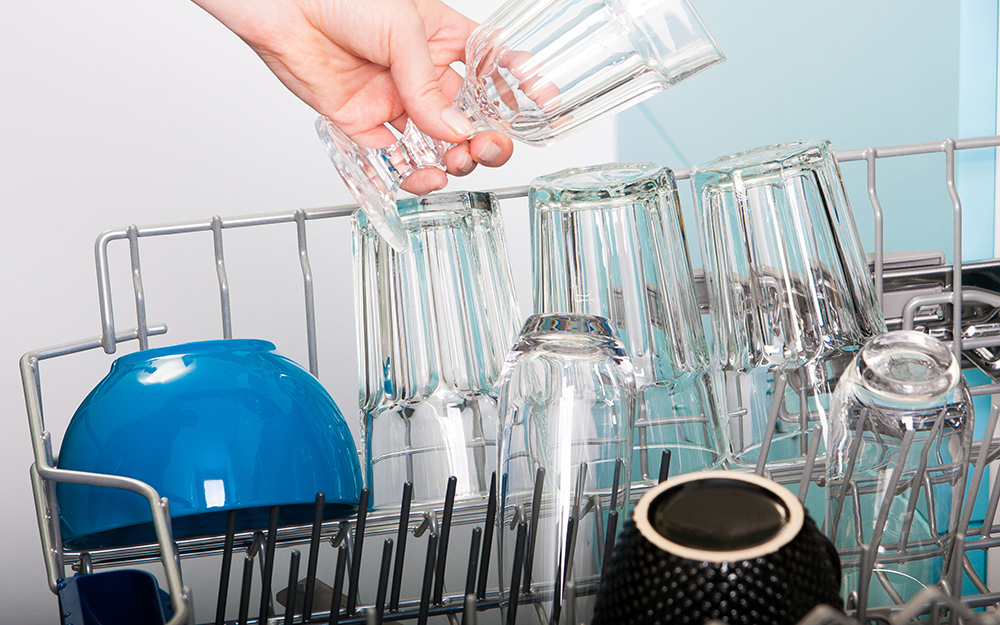 A person loading glasses into the top rack of a dishwasher