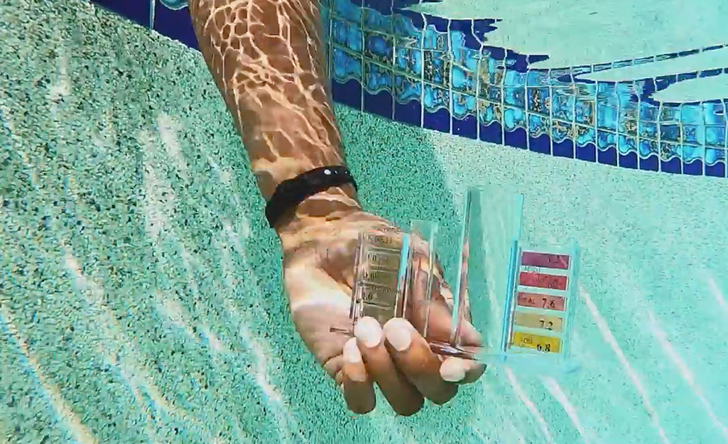 Someone collecting a pool water sample using a test kit.
