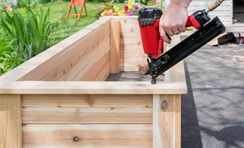 Person using nailer to assemble wood raised garden bed