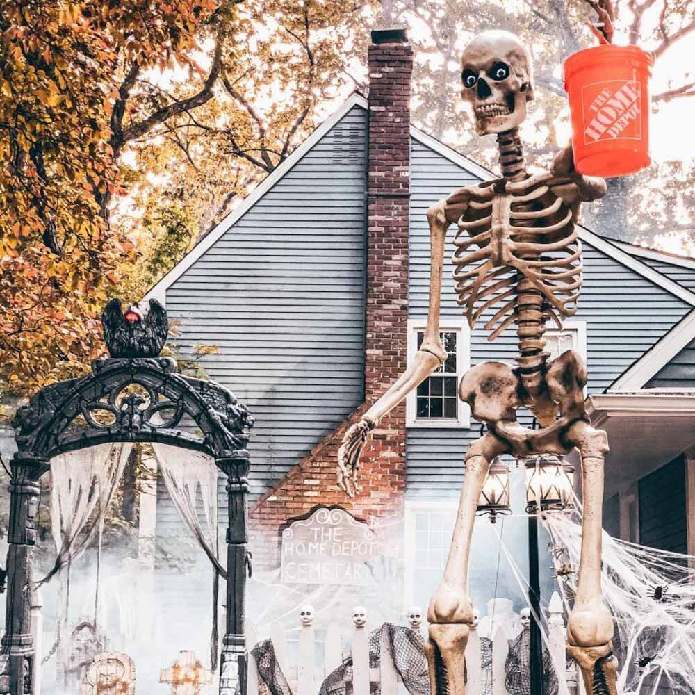 A 12-foot skeleton holding a Home Depot bucket in a decorated front yard.