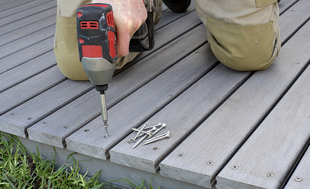 A person drives wood screws into a deck board with a power driver.