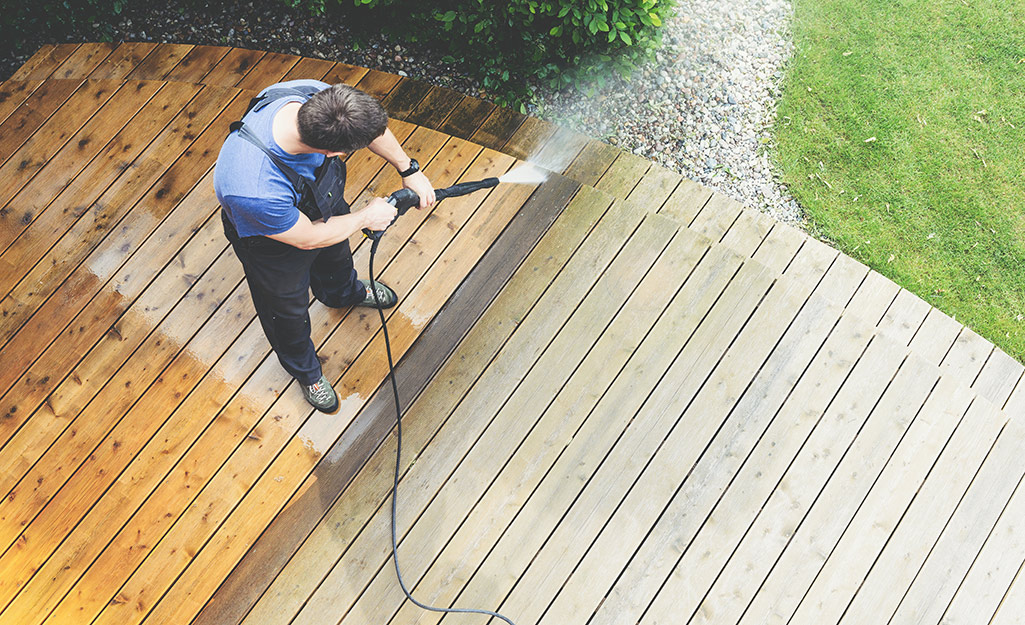 A person cleans a deck with a pressure washer.