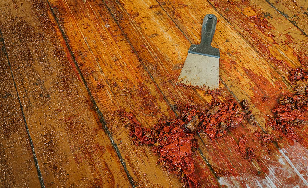 A paint scraper is next to part of a deck that has old finish scraped up.