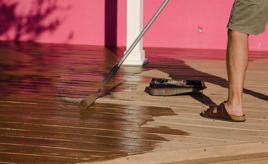 A person applies stain to a deck with a roller.