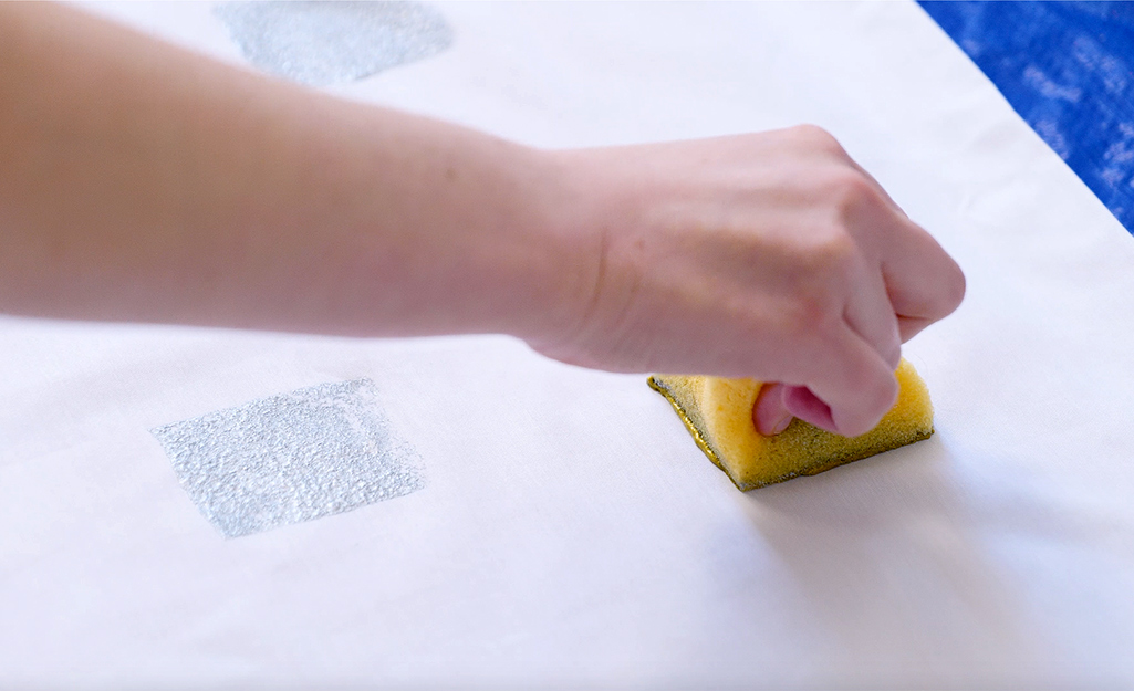 A person uses a sponge to stamp paint onto a pillowcase. A person uses a sponge to stamp paint onto a pillowcase.