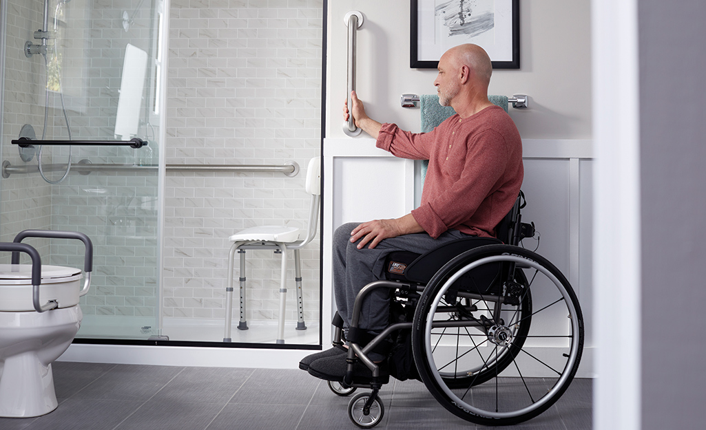 A man holding a grab bar in an accessible bathroom.