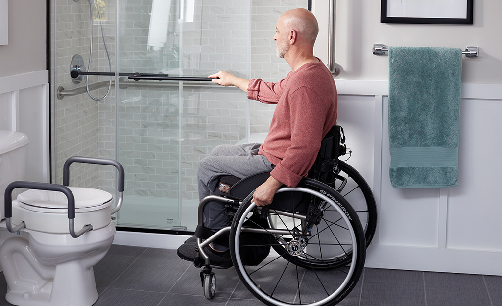 A man holding a shower bar in an accessible bathroom.