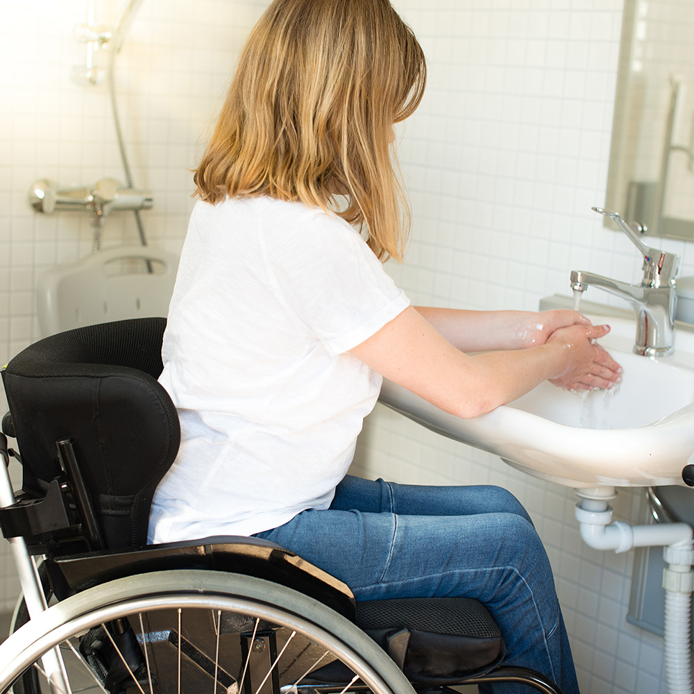 A person in a wheelchair washing their hands at a bathroom sink.