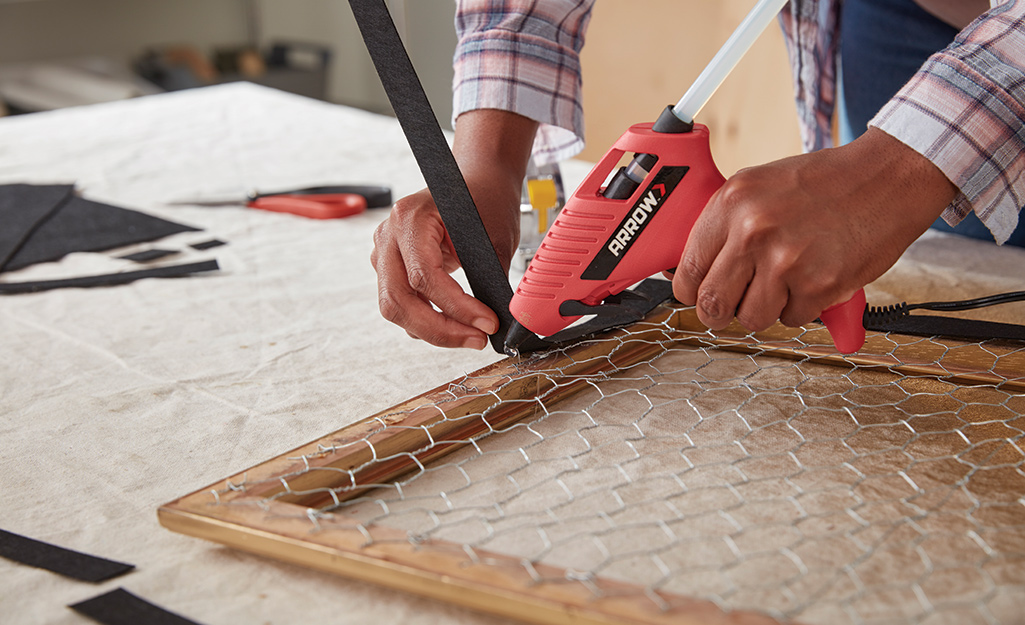 Person uses a glue gun to attach backing to frame