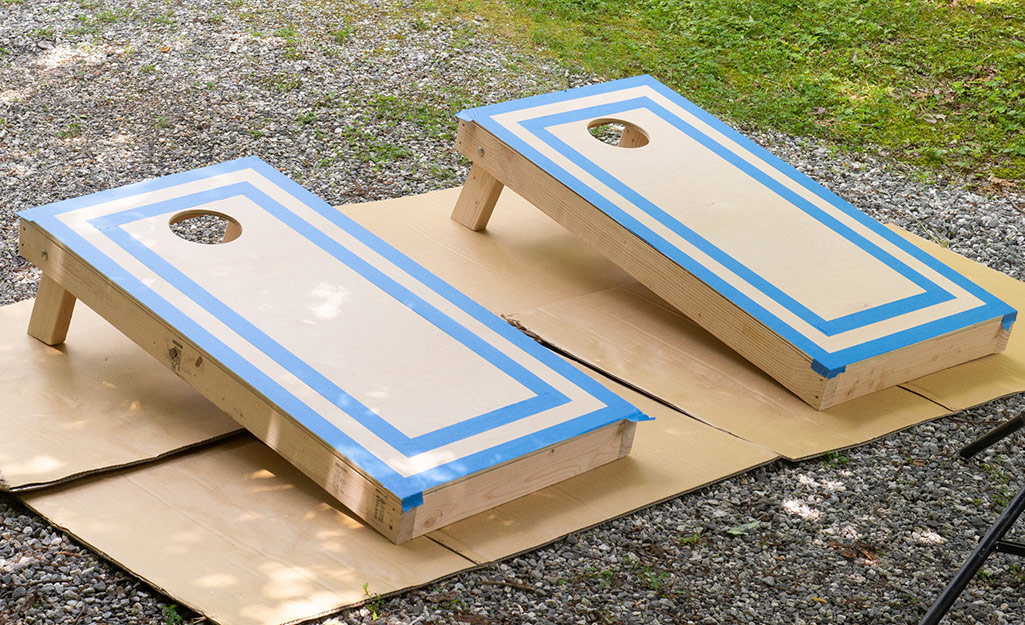 Taped off cornhole boards resting on cardboard waiting to be painted.