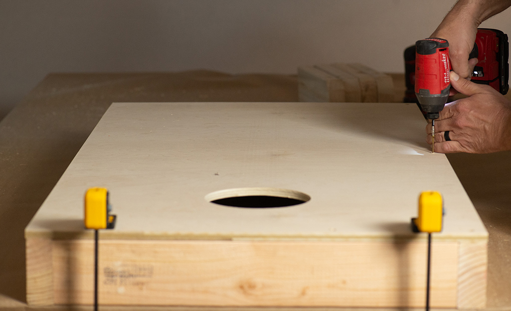 A person attaching the top of a cornhole board to its base.
