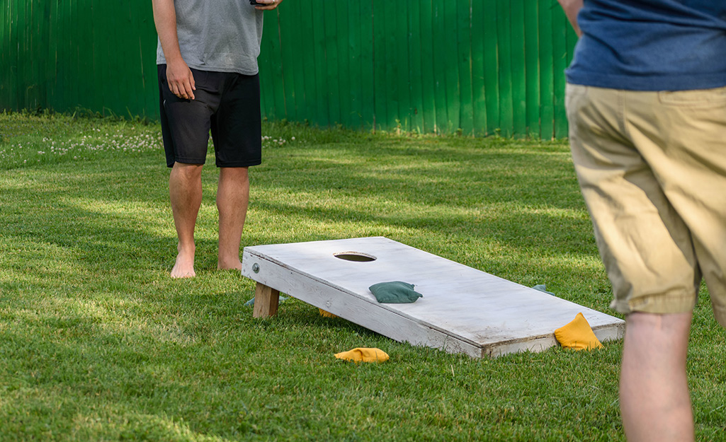 Two people playing cornhole on a lawn.