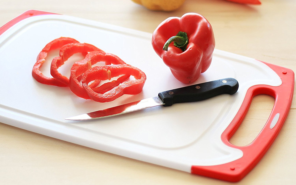 A white plastic cutting board with sliced bell peppers on top. 