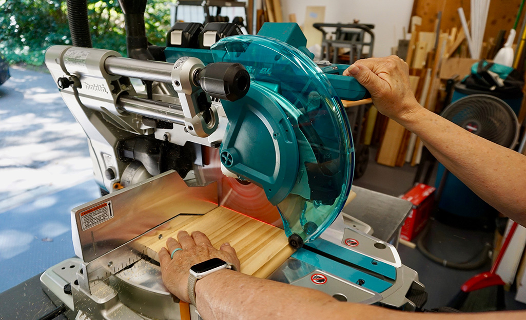 A worker uses a saw to cut through layered wood.