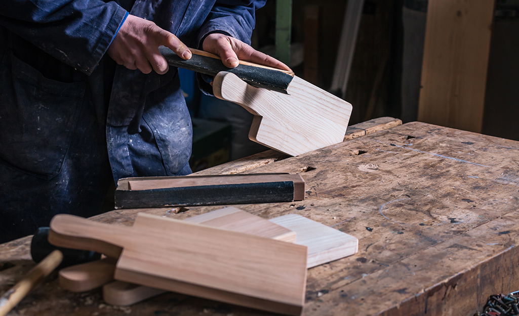 A worker uses sand paper on a cutting board handle.