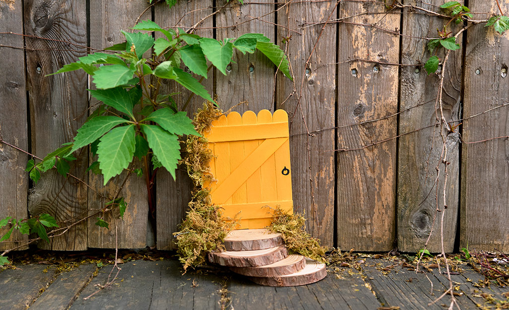 A tiny yellow door propped against a fence welcomes fairies. 
