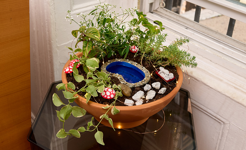 A fairy garden in a planter sits near a window inside a home.