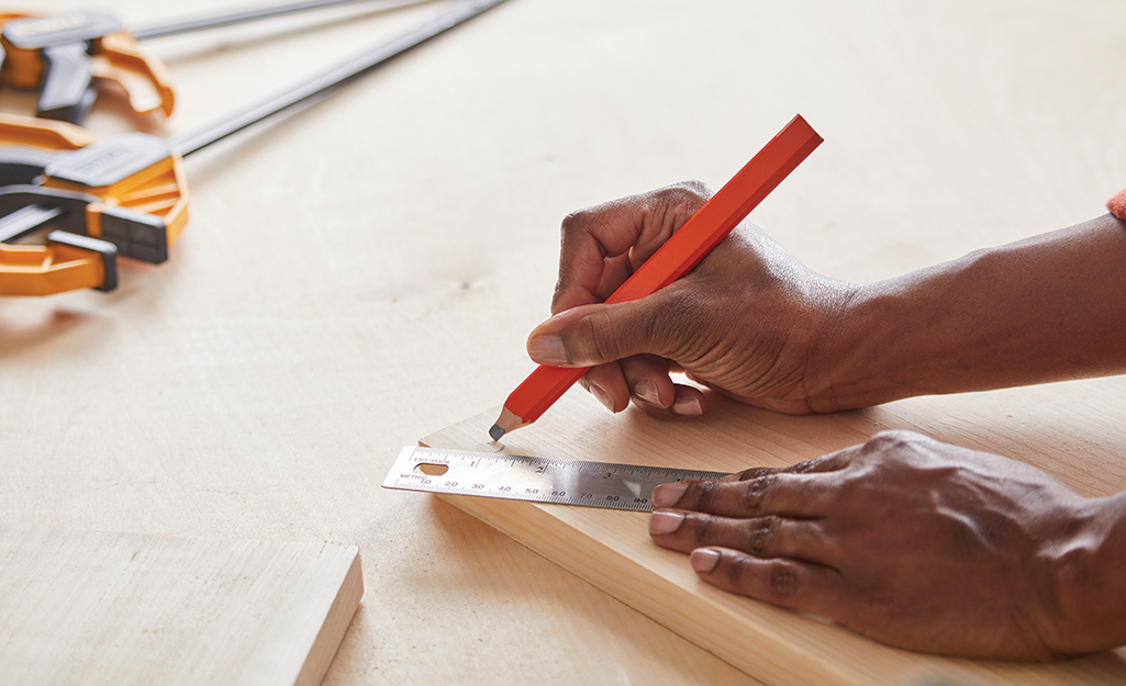 A person uses a pencil to draw a circular drill guide in the corner of a piece of wood.