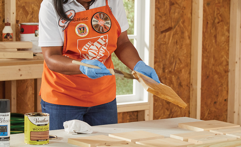 A woman applies stain to the pieces of wood that will be used to make a Halloween candy holder.